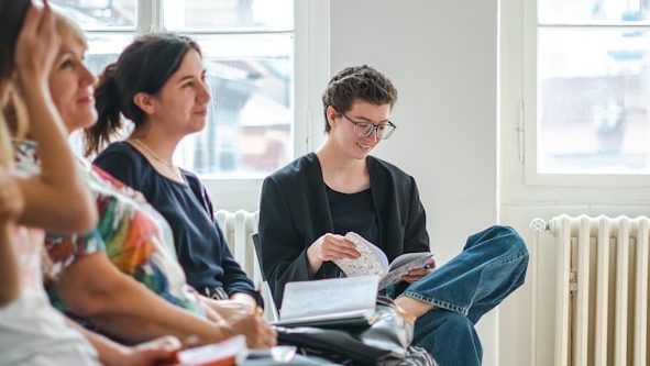 Workshop vor Ort Eine Gruppe von Personen sitzt in einem hellen Raum, eine Person liest aufmerksam in einem Buch.