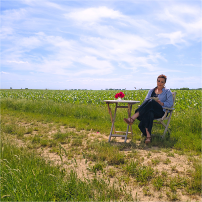 Karen schreibend im Grünen Frau sitzt an einem Tisch mit Blumenvase in einer grünen Feldlandschaft.