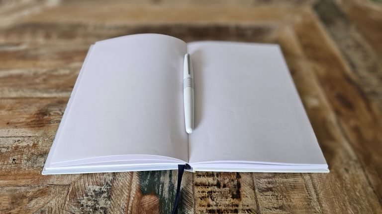 Schreiben wirkt Ein geöffnetes Notizbuch mit leeren Seiten auf einer holzigen Oberfläche.
