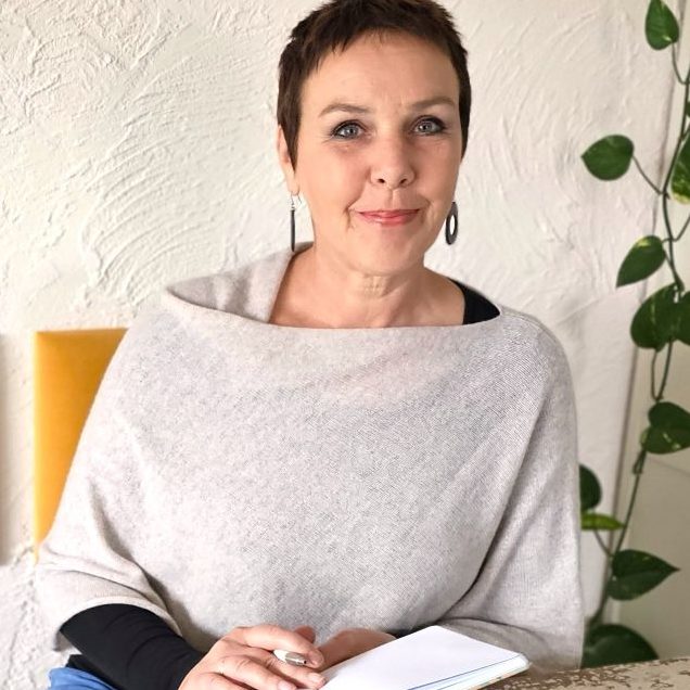 Karen schreibend Frau mit kurzer Frisur, die in ein Notizbuch schreibt, umgeben von Pflanzen und einer Tasse Tee.
