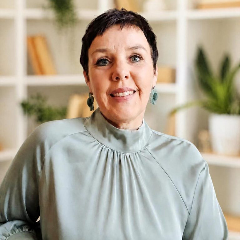 Frau mit kurzer Frisur, die in ein Notizbuch schreibt, umgeben von Pflanzen und einer Tasse Tee.